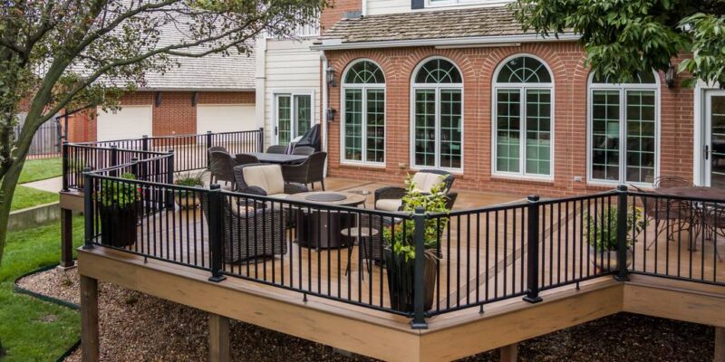 A large wooden patio deck with fire pit and dark wicker furniture by Farha Home Trends.