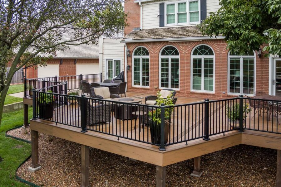 A large wooden patio deck with fire pit and dark wicker furniture by Farha Home Trends.