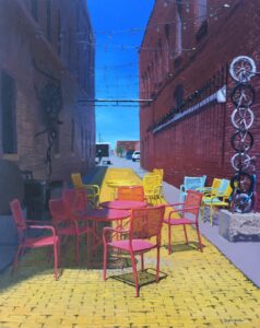 A painting of Gallery Alley consisting of an alley with a yellow brick pathway with tables and chairs. By local artist Bill Goffrier.