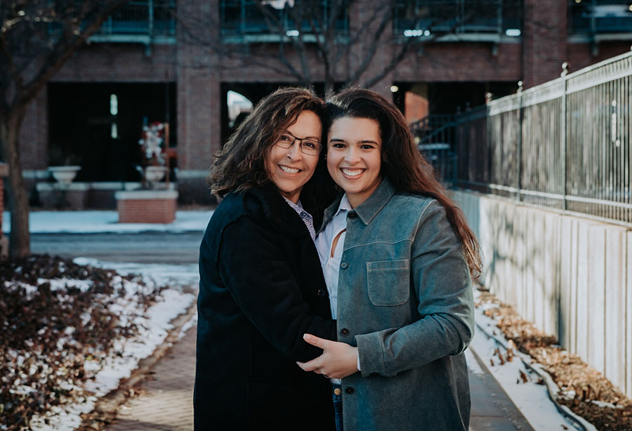 Aida and her daughter, Jamilla, standing on city sidewalk embracing and smiling